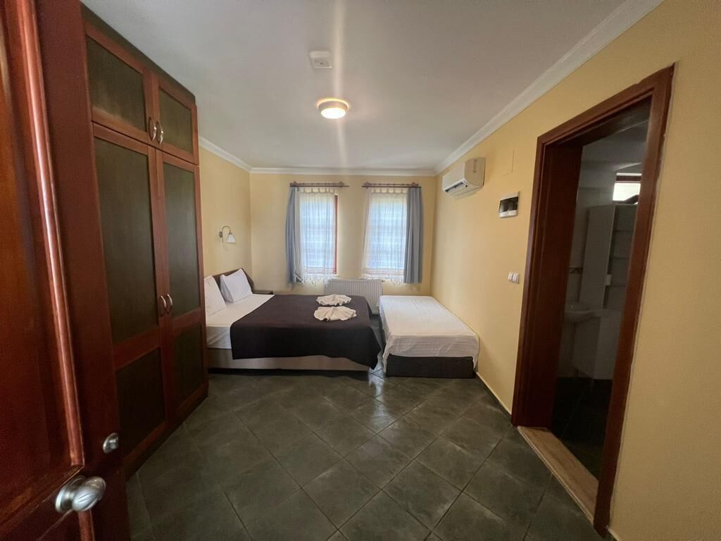 Ein Zimmer mit zwei Betten, einem Holzschrank, einer Deckenleuchte und einem fenster mit Vorhängen.