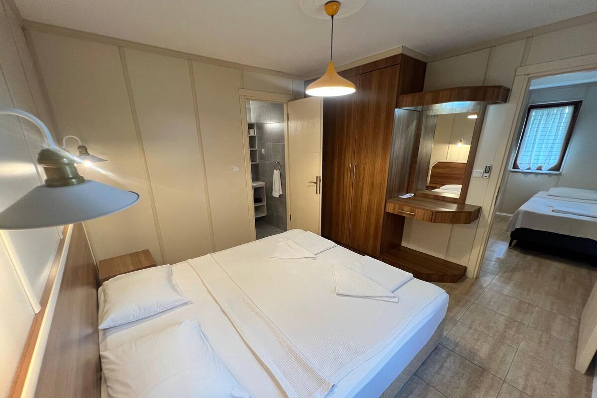 A hotel room with a bed, a wooden wardrobe, a bathroom, and a small desk with a mirror.