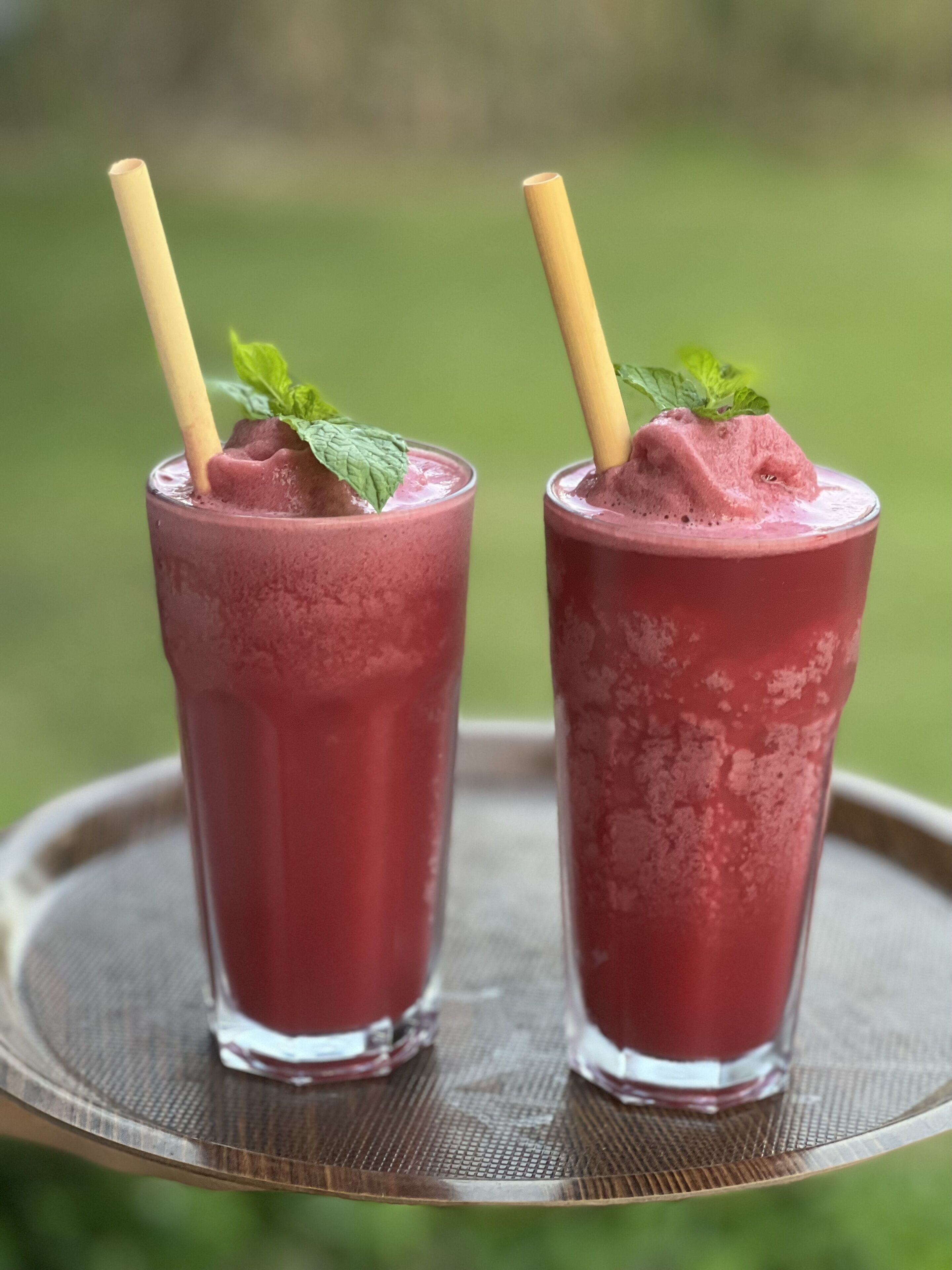 Two tall glasses of pink smoothie with mint leaves on a round tray.