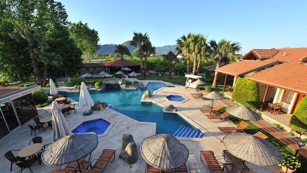 A resort pool area with multiple pools, lounge chairs, umbrellas, and a view of the mountains. - Grenadine Lodge (Ortaca)