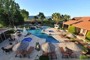 A resort pool area with multiple pools, lounge chairs, umbrellas, and a view of the mountains. - Grenadine Lodge (Ortaca)