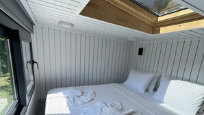 A modern bedroom with a skylight, a large bed with white bedding, and a wooden floor. - Grenadine Lodge (Ortaca)
