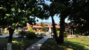 A resort with a stone pathway leading to a pool area, surrounded by trees and buildings with red roofs. - Grenadine Lodge (Ortaca)