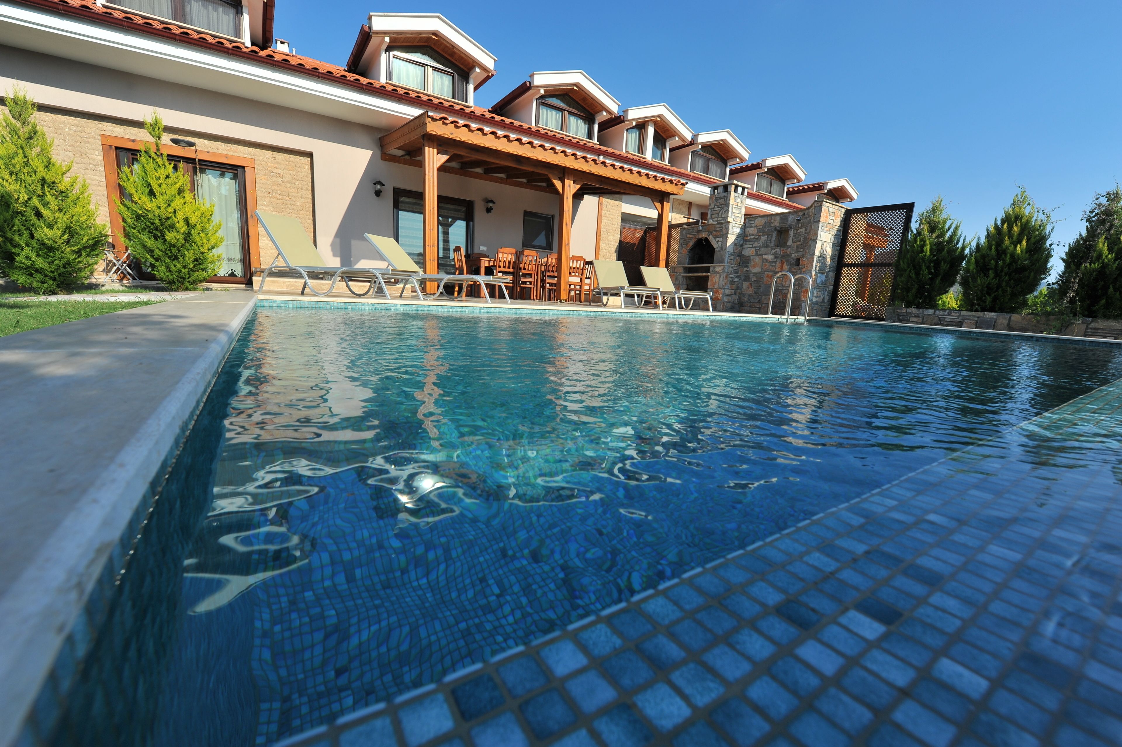 Una piscina con sillones de descanso y un porche cubierto.