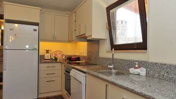 A compact kitchen with a refrigerator, dishwasher, and a window with blinds.