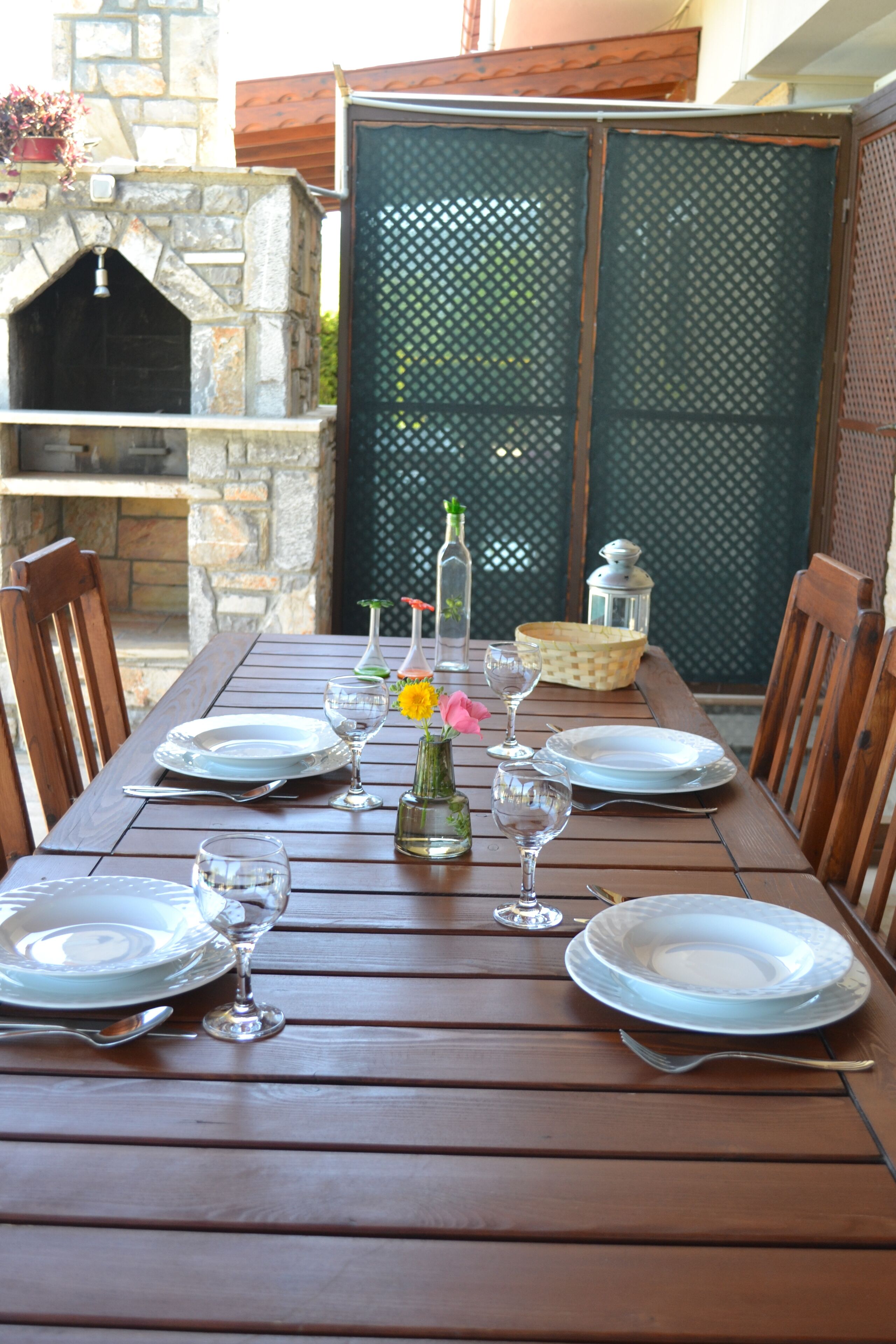 A wooden dining table set with plates, glasses, and cutlery, surrounded by chairs.