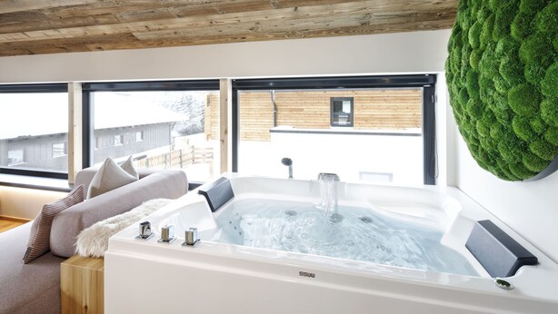 Ein modernes Badezimmer mit einer großen Badewanne, einer Holzbeschichtung an der Decke und Blick auf ein Gebäude.
