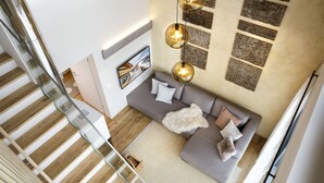 Ein modernes Wohnzimmer mit grauem Sofa, einer Holztreppe und einer Wandleuchte.