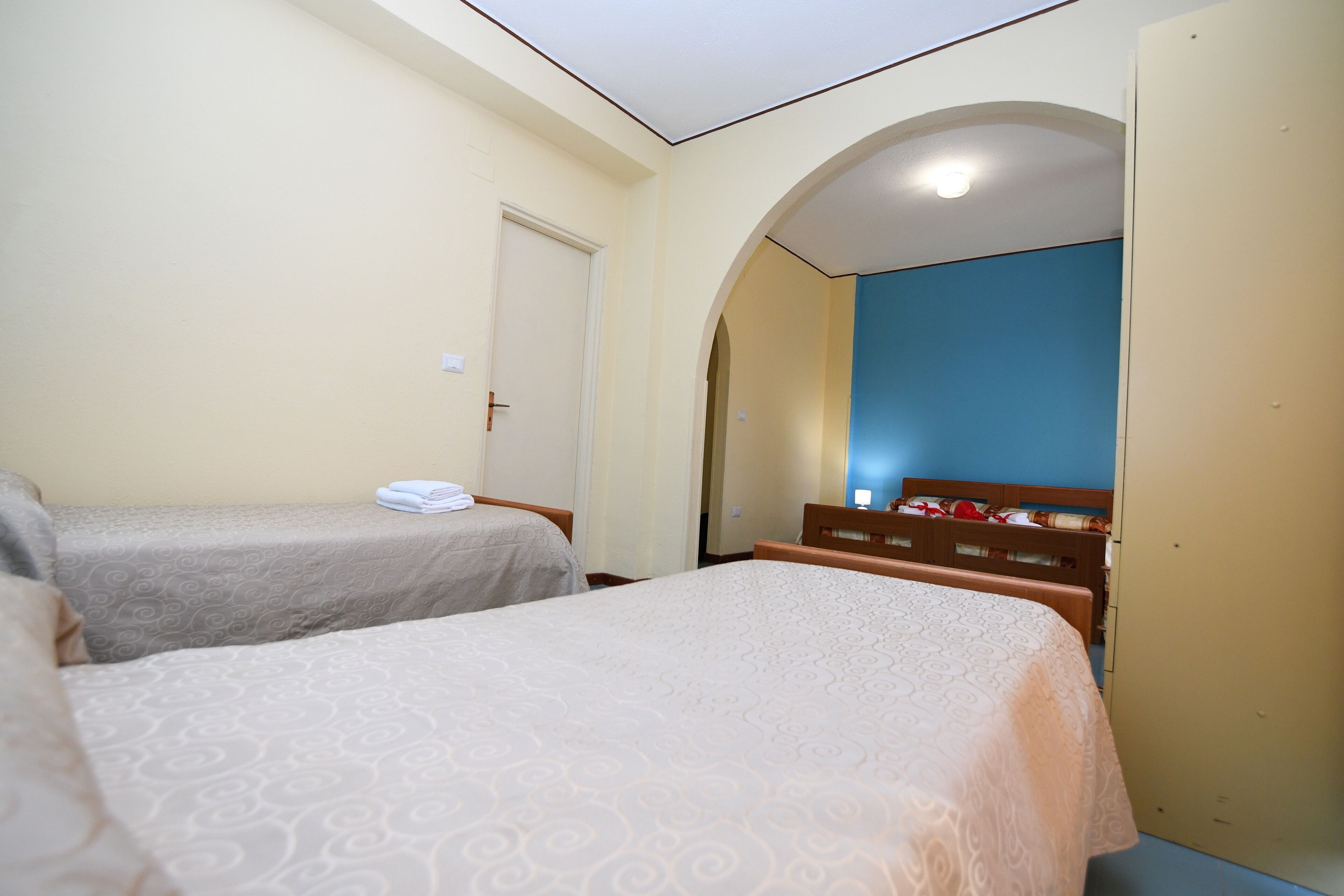 A hotel room with two single beds, a wardrobe, and a bathroom visible through an arched doorway.