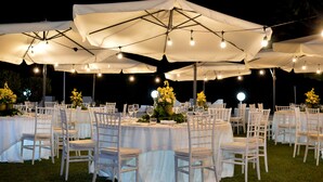 A formal outdoor dining area with round tables, white chairs, and large umbrellas.