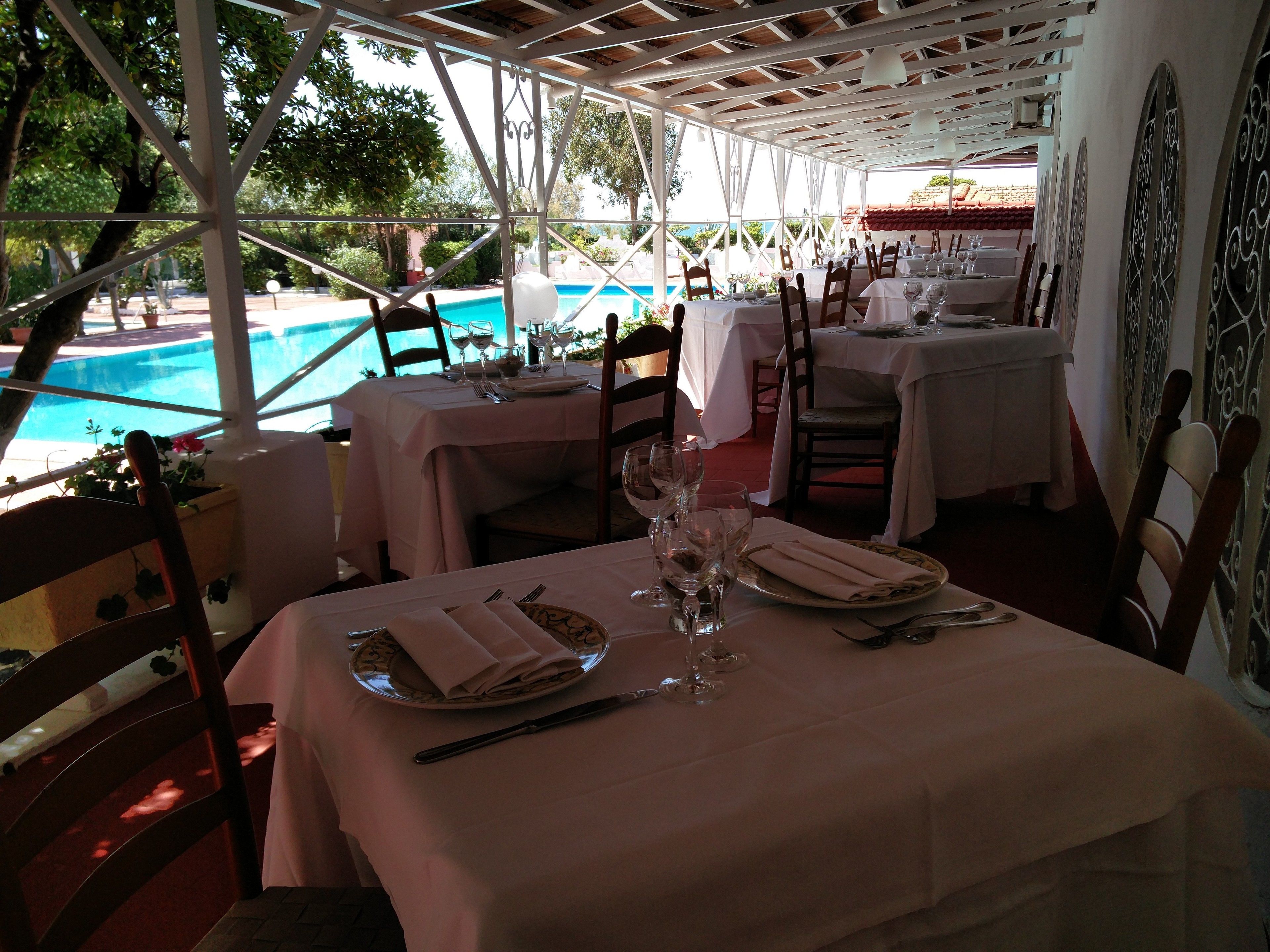 Un área de comedor al aire libre con mesas preparadas para dos, con vista a una piscina.
