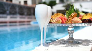 A poolside setting with a glass table holding a fruit platter and two white glasses.