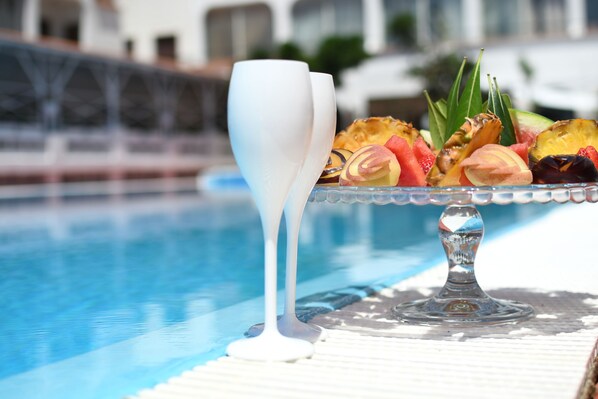 A poolside setting with a glass table holding a fruit platter and two white glasses.
