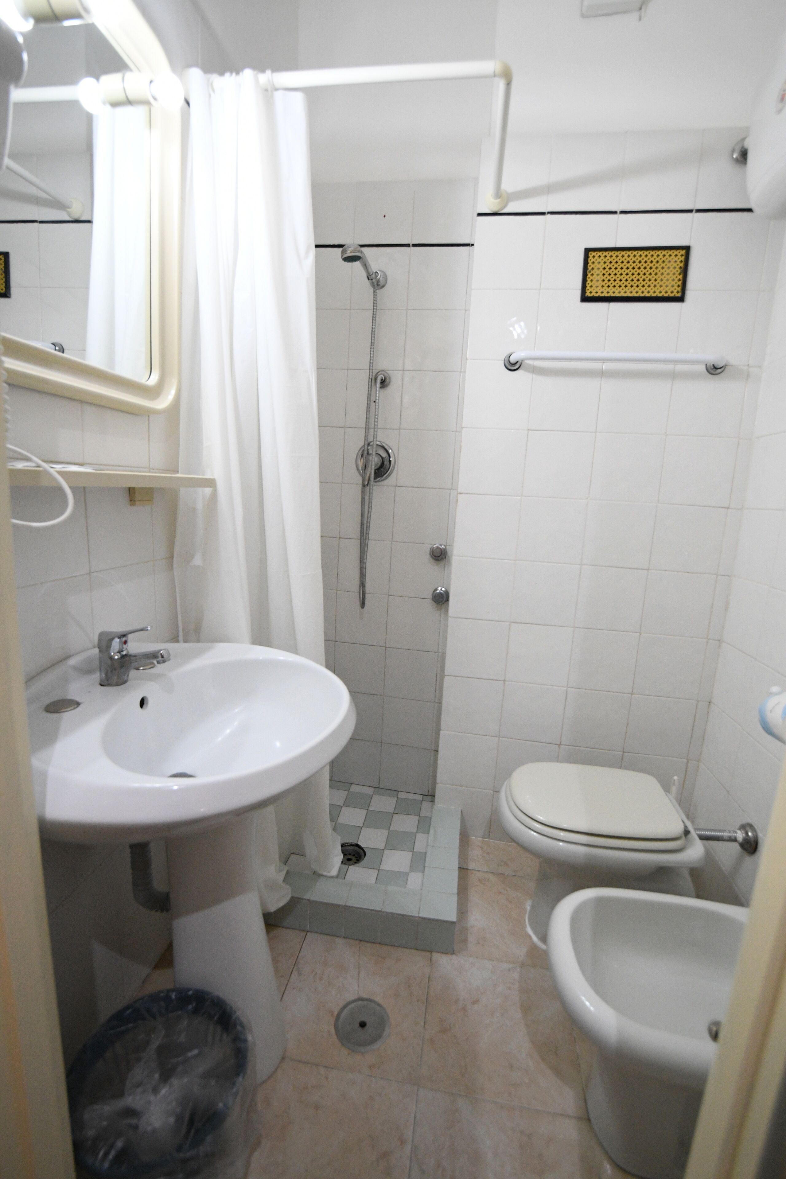 A bathroom with a sink, toilet, bidet, shower, and a towel rack.