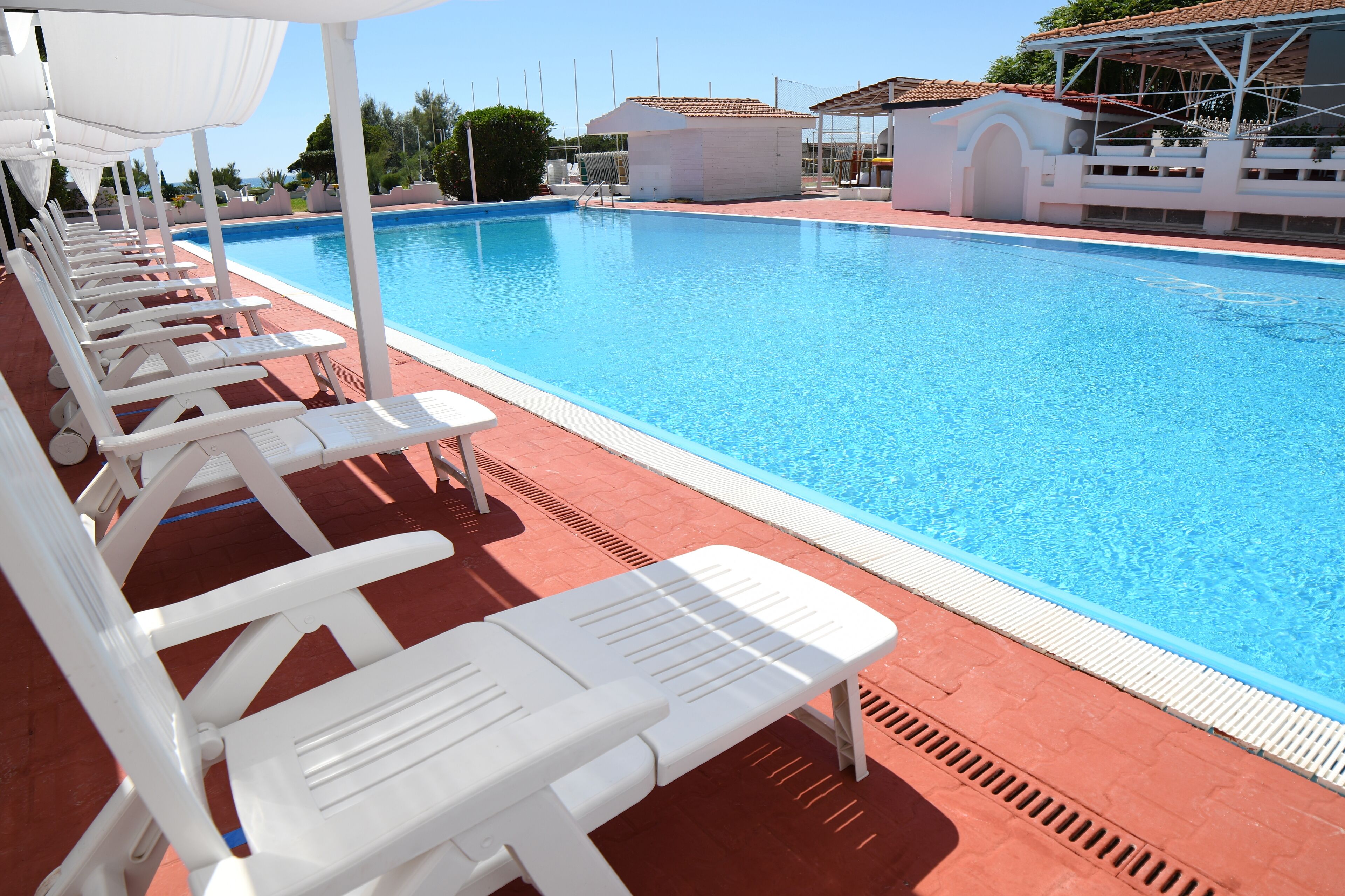 Una piscina con sillas de descanso blancas y una zona cubierta.
