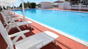 Una piscina con sillas de descanso blancas y una zona cubierta.