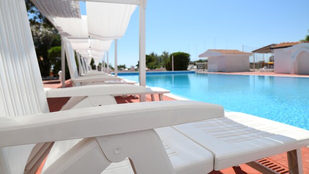 A row of white lounge chairs by a pool with a clear blue sky in the background.