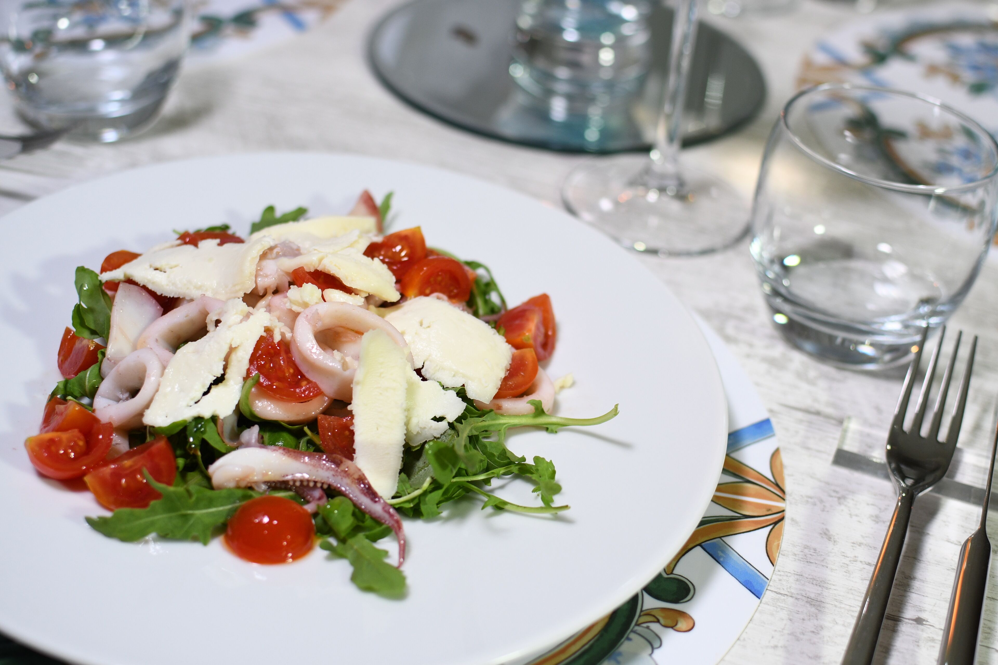 A plate of salad with tomatoes, cheese, and greens on a table.