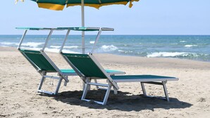 A beach with two green lounge chairs under a striped umbrella.