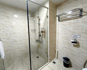 A modern bathroom with a glass-enclosed shower, a towel rack, and a trash bin.