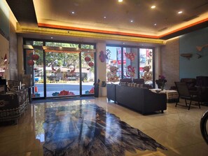 Un vestíbulo de hotel con mostrador de recepción, zona de estar y grandes ventanales con detalles decorativos.
