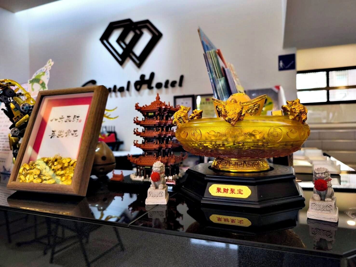 L’intérieur d’un hôtel, avec un comptoir d’accueil, un certificat encadré, un bol décoratif doré et des éléments d’architecture chinoise traditionnelle.
