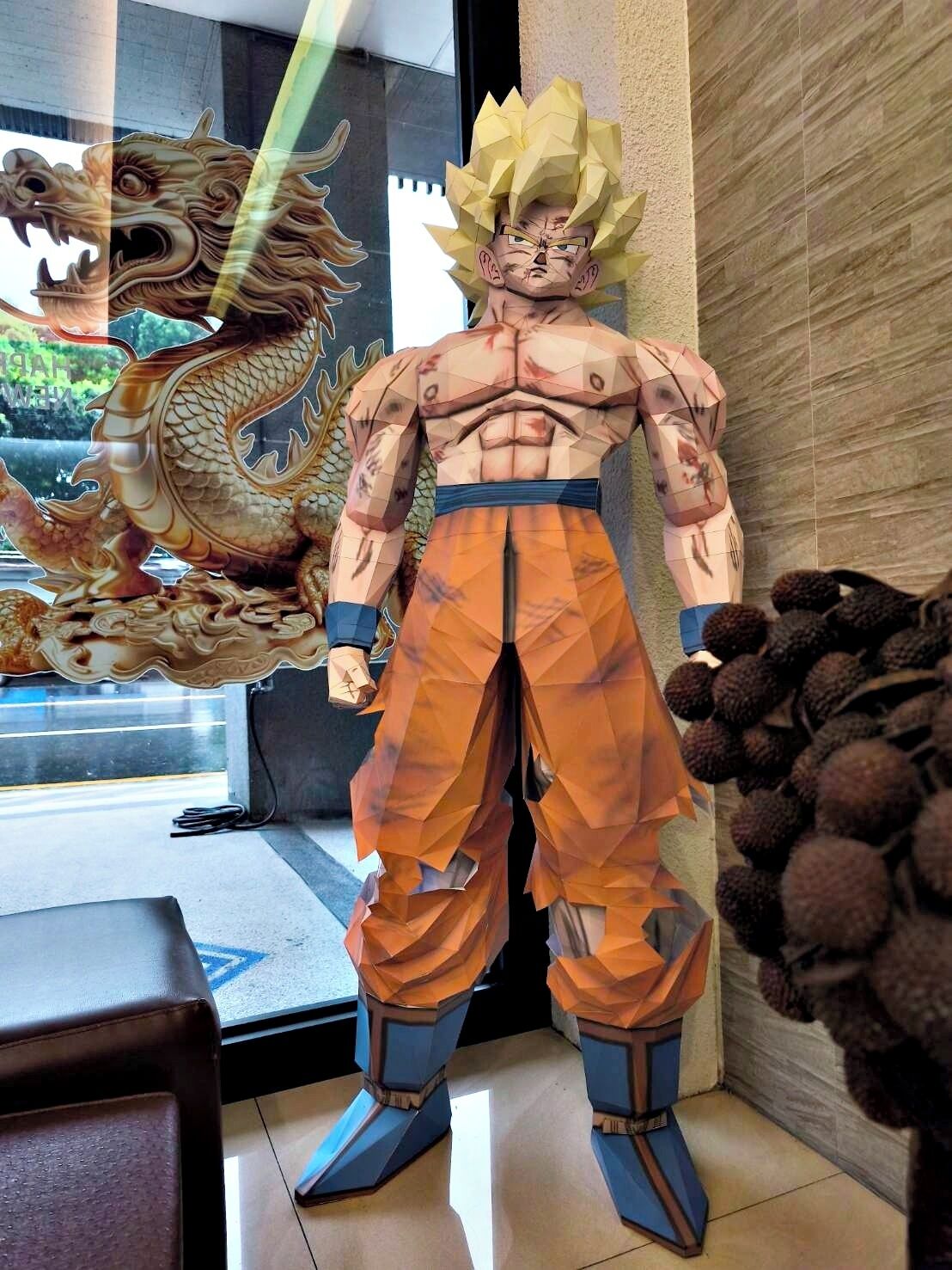 A statue of a muscular character with spiky hair and orange pants, standing indoors with a dragon in the background.