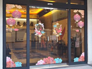A storefront with large glass windows, decorative paper cutouts of flowers, and hanging lanterns.
