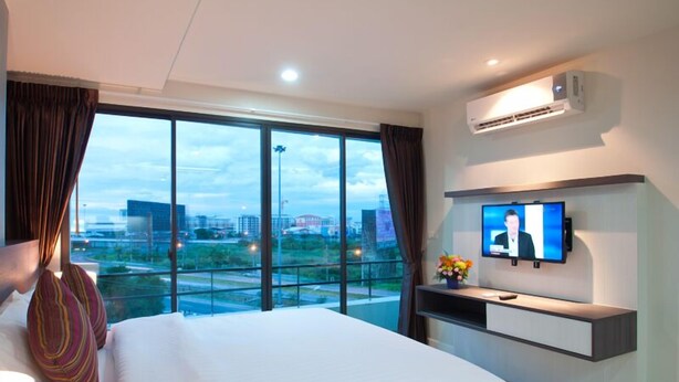 Habitación de hotel con una cama grande, un televisor y vistas de la ciudad a través de amplias ventanas.
