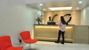 Un área de recepción con un mostrador de madera, un arreglo floral y dos sillones naranja.