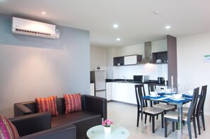 A modern living room with a sofa, a dining table set for four, and a kitchen in the background. - VC Residence (Chonburi)