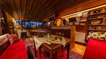 Una habitació acollidora amb sostre de fusta, una taula de dinar amb cambrera de puntes, un sofà vermell i una biblioteca amb diversos objectes.