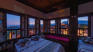 Un dormitorio con ventanas amplias, una cama con colcha estampada, una mesita de noche y un banco.
