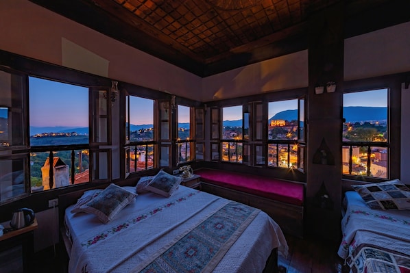 Ein Schlafzimmer mit großen Fenstern, einem Bett mit gemustertem Überwurf, einem Nachttisch und einer Bank.