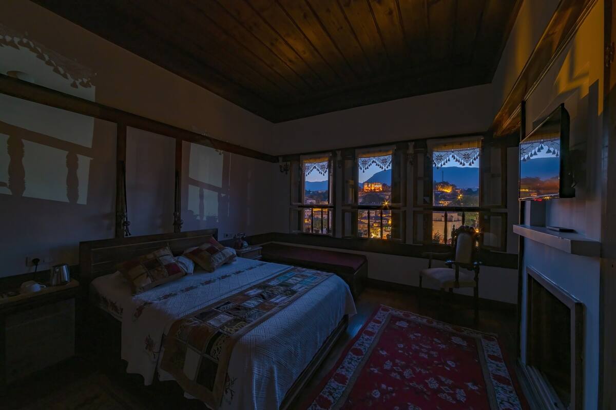 Un dormitorio con una cama grande, techo de madera y vistas a un paisaje urbano a través de ventanas.