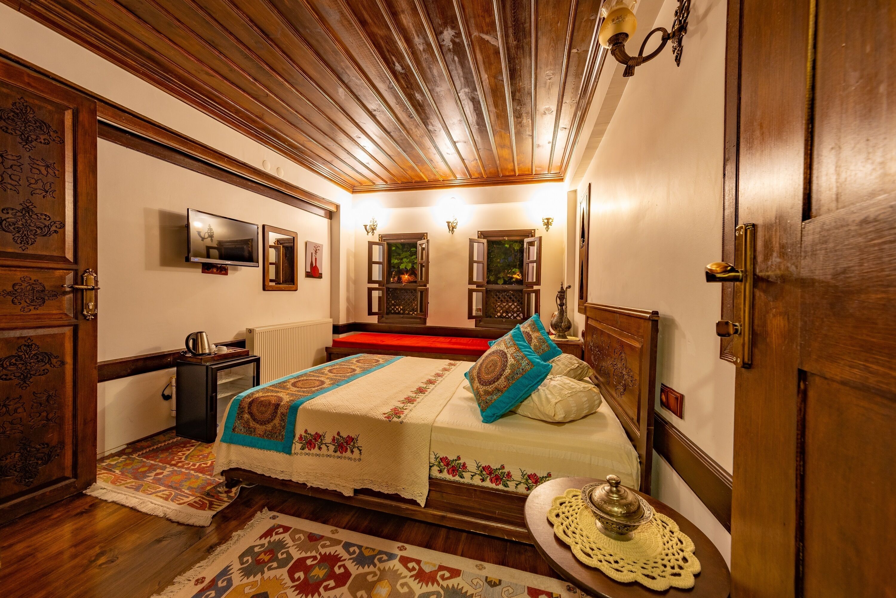 A traditional room with a wooden ceiling, a bed with patterned bedding, a small table with a decorative item, and a television on the wall.