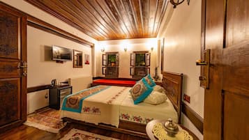 A traditional room with a wooden ceiling, a bed with patterned bedding, a small table with a decorative item, and a television on the wall.