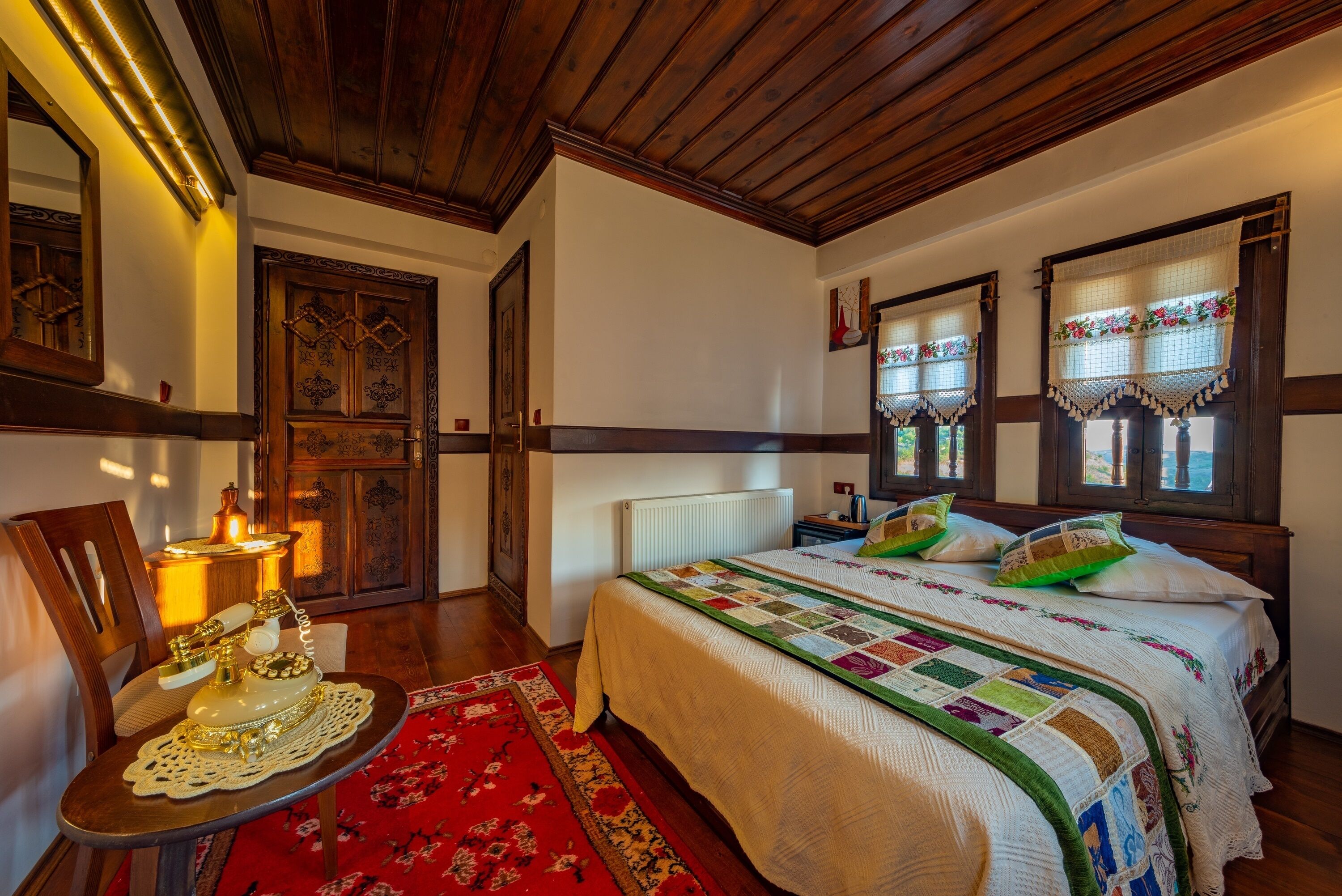 A bedroom with a wooden ceiling, a large bed with a quilt, a nightstand, a dresser, and a red rug.