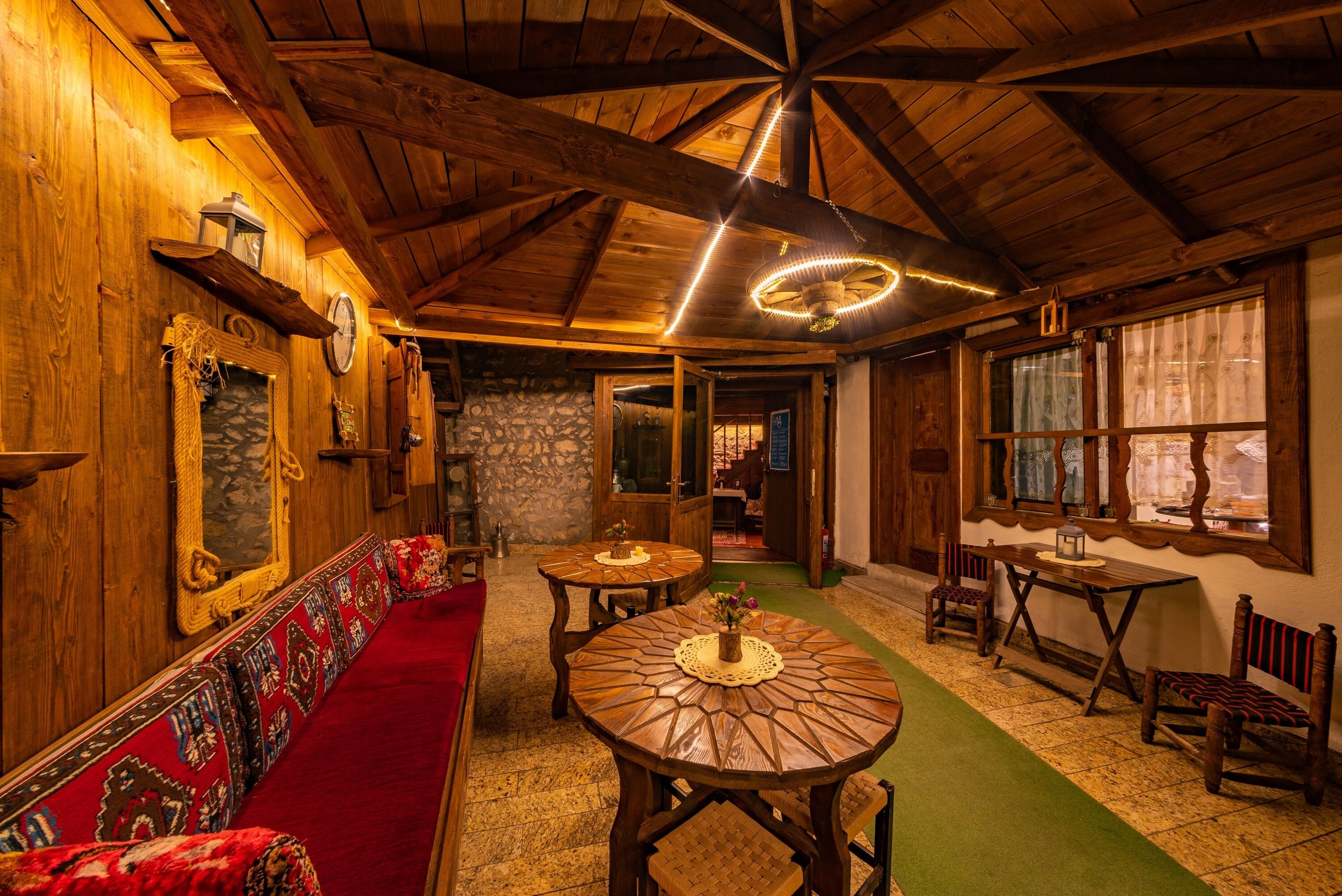 A cozy interior with wooden beams, a stone wall, a red bench, and a green carpet.