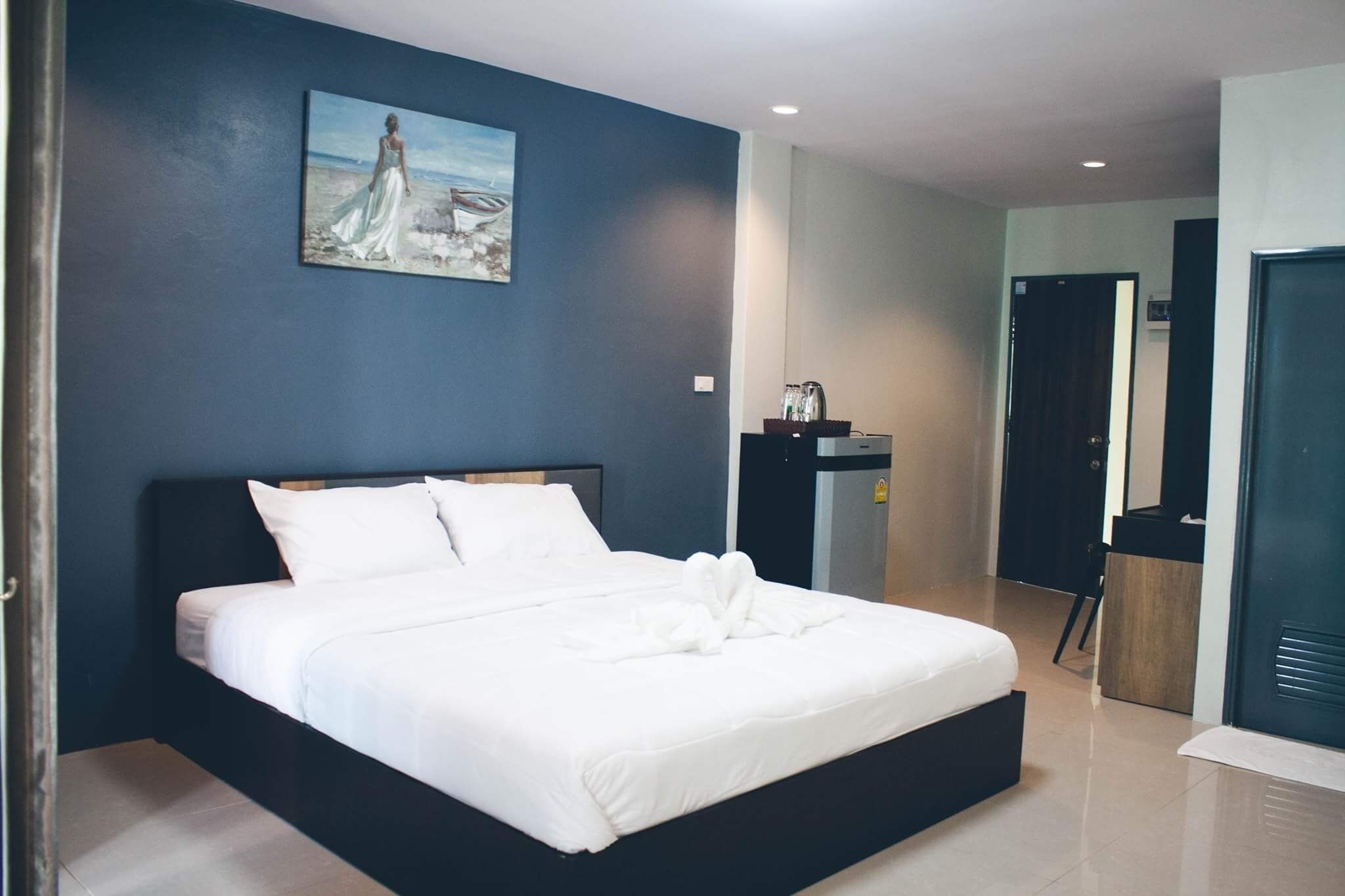 A modern hotel room with a large bed, a painting on the wall, a desk with a chair, and a door.