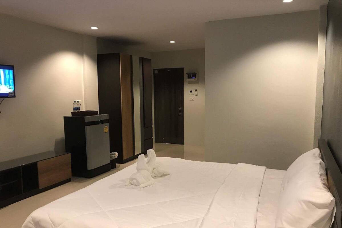 A hotel room with a large bed, a TV mounted on the wall, a minibar, and a door leading to another room.