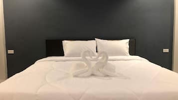 A neatly made bed with a white duvet and two pillows, a dark headboard, and a wall with a switch.