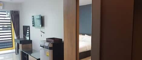 Una habitación de hotel con cama, escritorio, silla, televisor y ventana con cortinas.