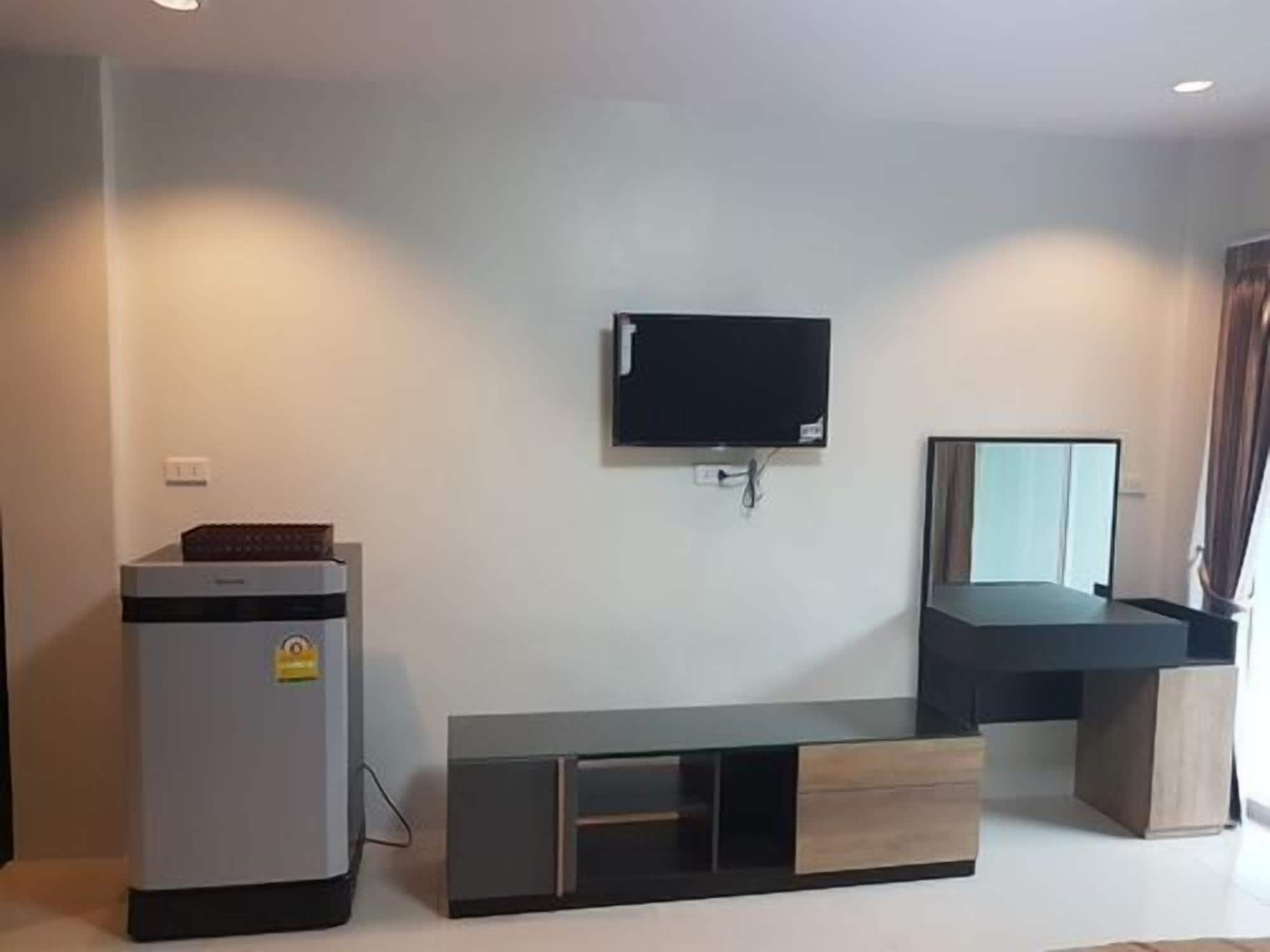 A modern room with a flat-screen TV mounted on the wall, a small refrigerator, and a wooden console table.