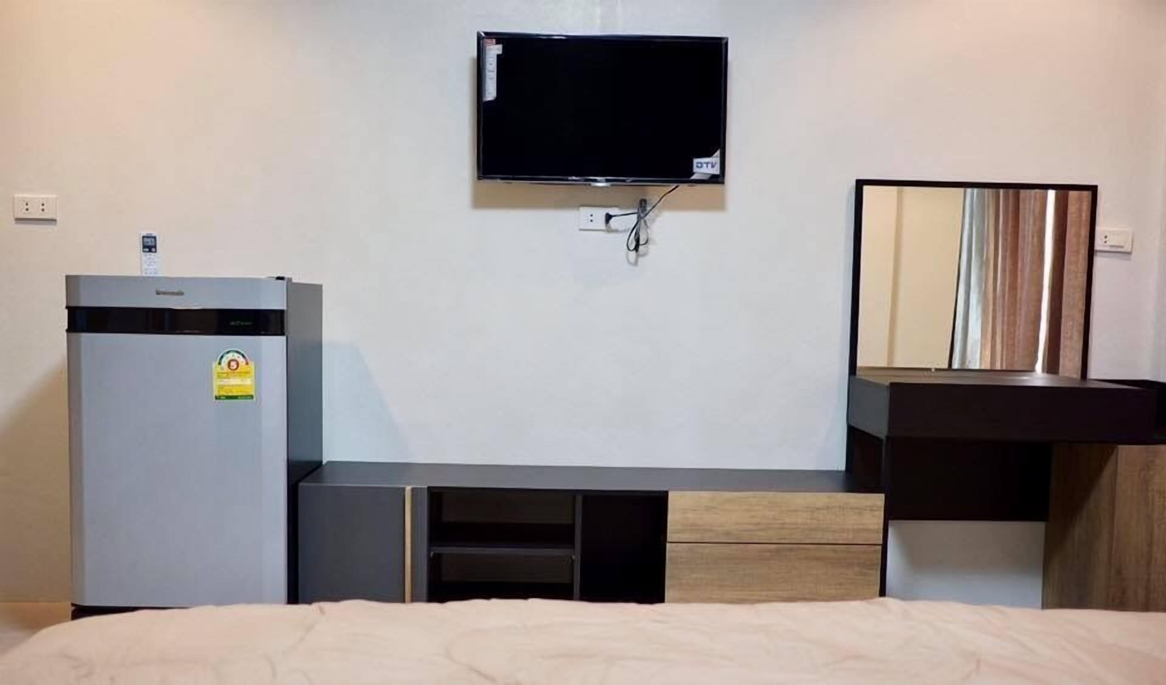 A hotel room with a bed, a minibar, a television mounted on the wall, and a mirror above a sink.