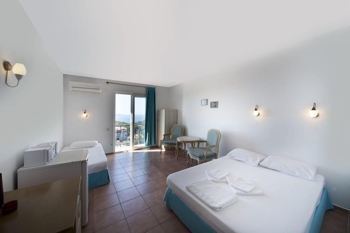 Habitación de hotel con cama, escritorio, silla, mesita y balcón con vistas.