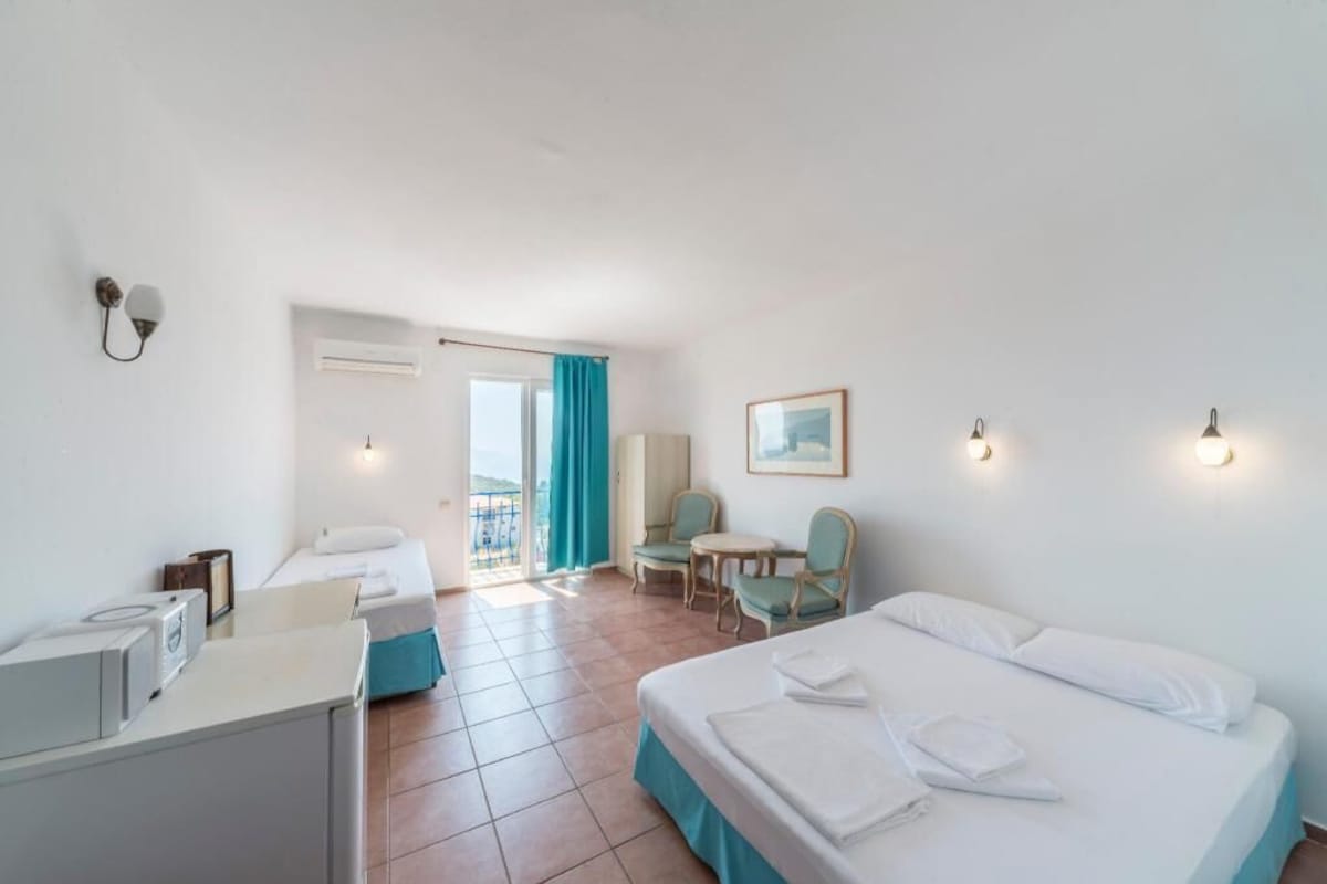 Habitación de hotel con dos camas, un escritorio, una silla, una mesita y un balcón con vistas.