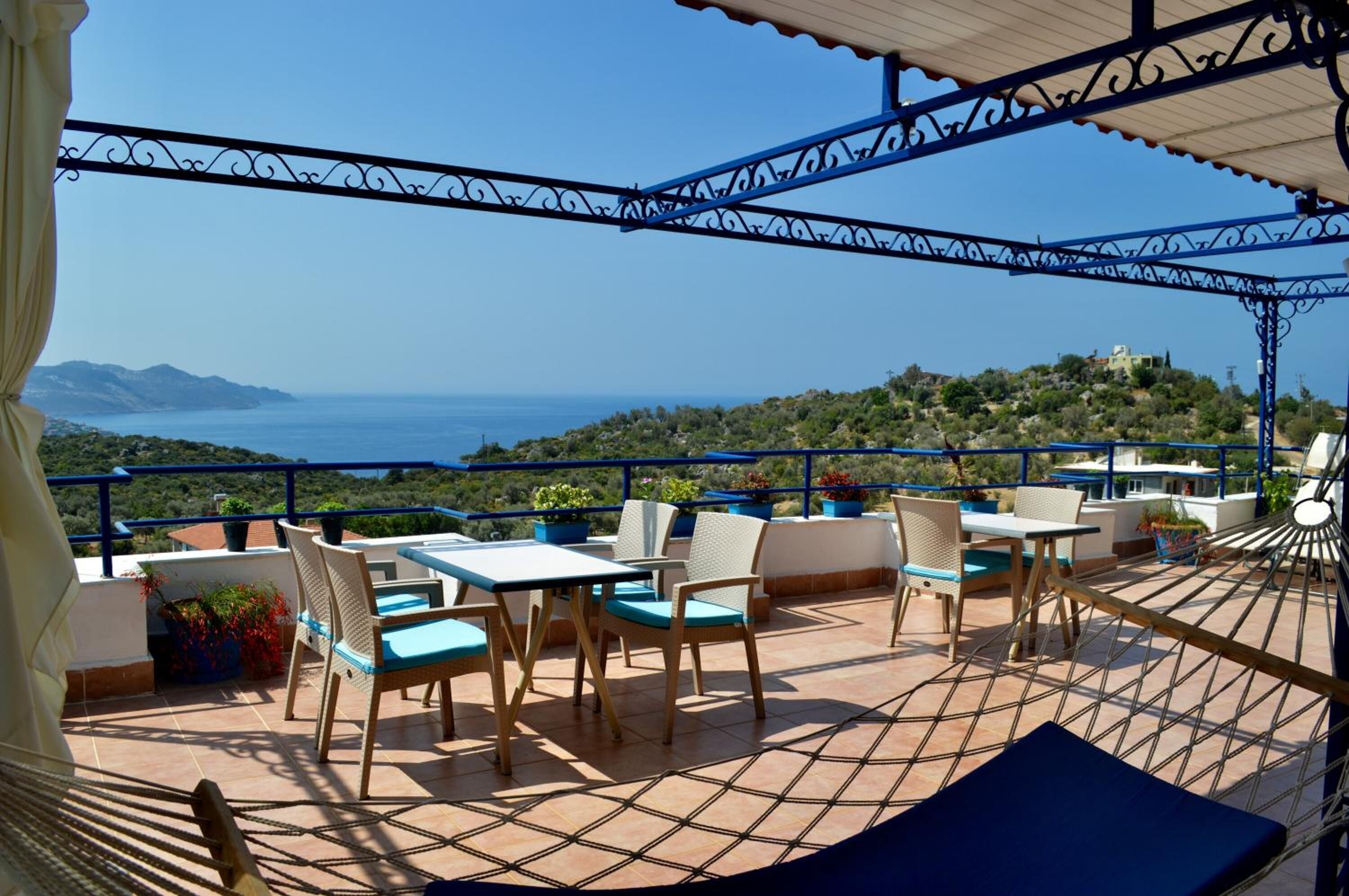 A terrace with outdoor seating, a hammock, and a view of the sea and hills.