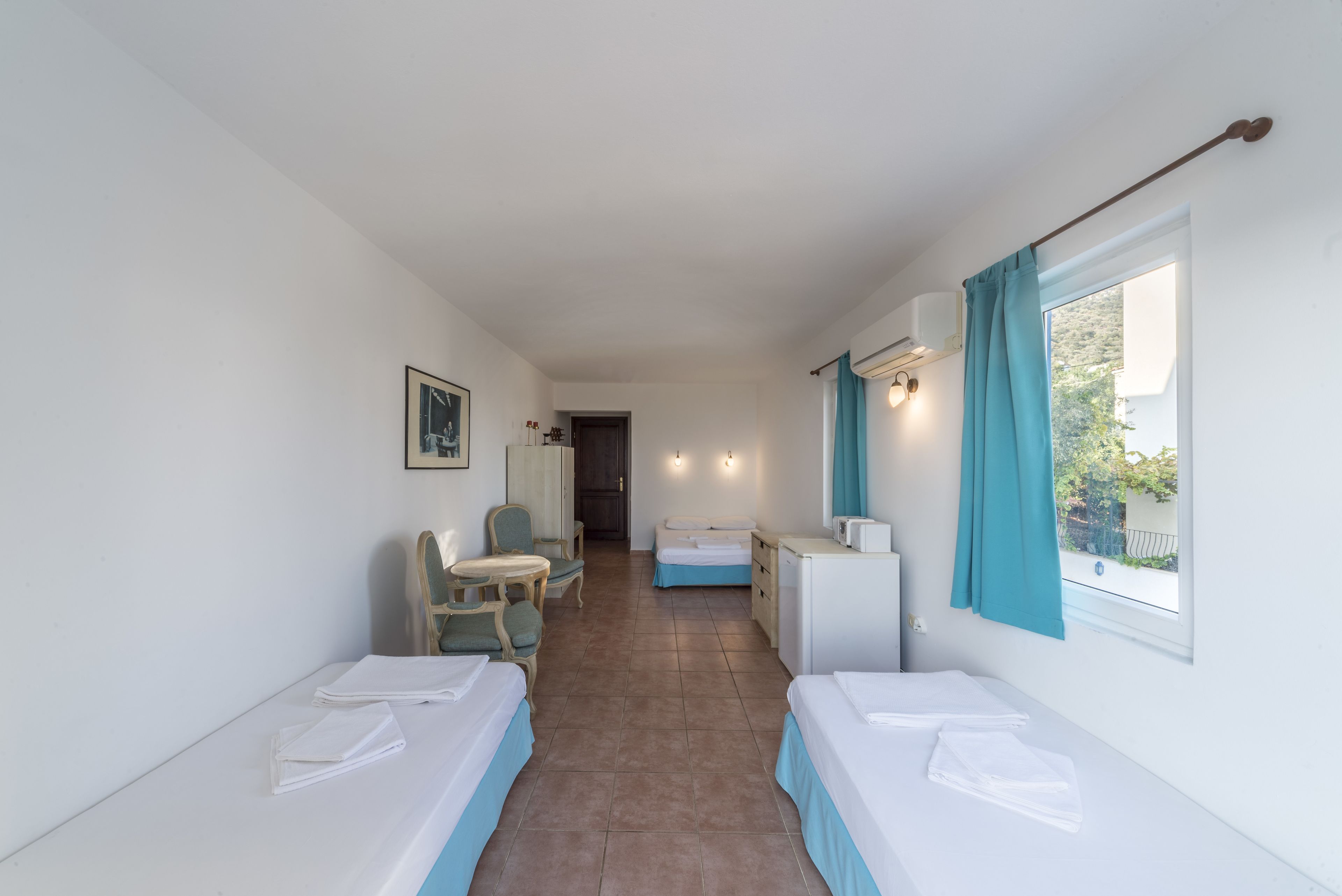 Una camera d'albergo con due letti singoli, una scrivania, una sedia, un tavolino e una finestra con tende.