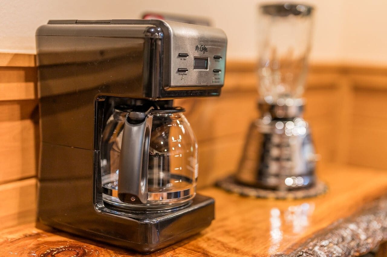 Eine Kaffeemaschine mit digitaler Anzeige und einem Glasbehälter auf einer Holzoberfläche.